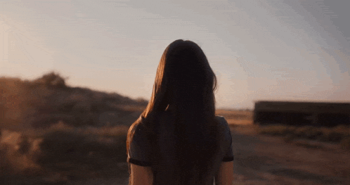 a woman with long hair is standing in a field with her back to the camera
