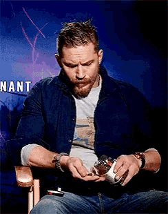 a man with a beard is sitting in front of a sign that says nant .