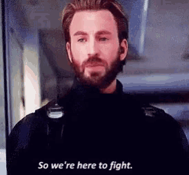 a man with a beard is standing in a room and saying `` so we 're here to fight . ''