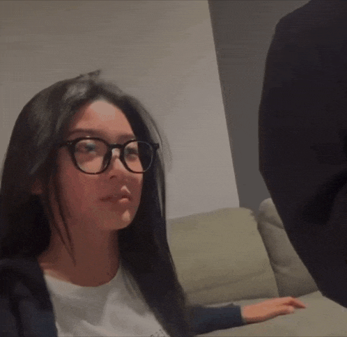 a woman wearing glasses is sitting on a couch and looking at the camera