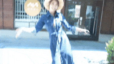 a woman in a blue dress and straw hat stands in front of a building with chinese writing