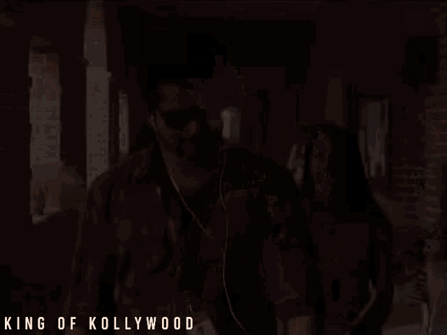a man wearing sunglasses and a lanyard that says king of kollywood walks down a hallway
