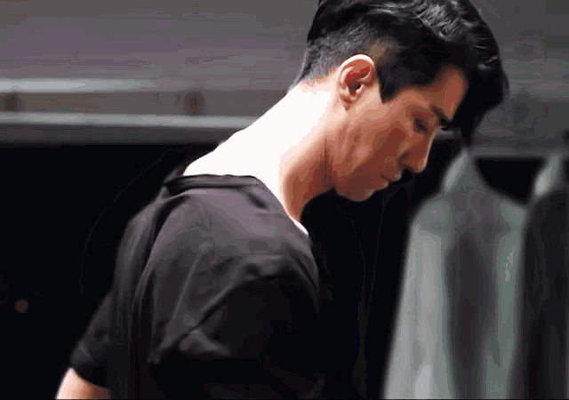 a man in a black shirt is looking down in a closet