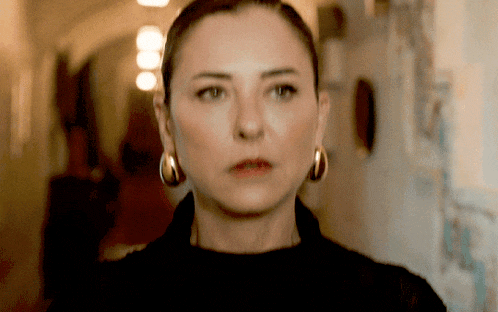 a woman wearing hoop earrings looks at the camera with a serious look on her face
