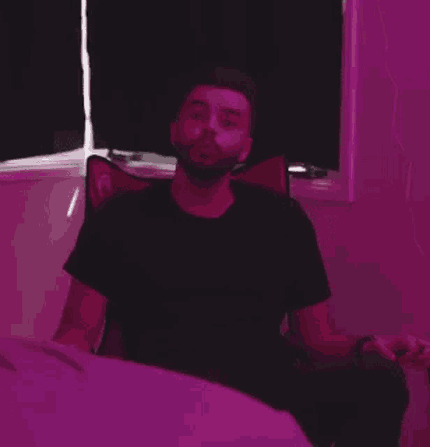 a man in a black shirt is sitting in a chair in front of a window in a room with purple lights .