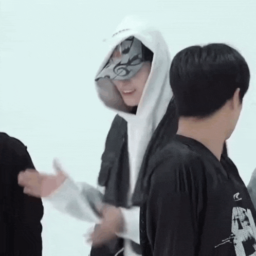 a man wearing a white hoodie and a hat is standing next to another man in a black shirt .