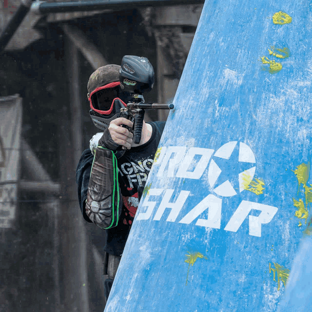 a person holding a paintball gun in front of a sign that says ' rx shar '