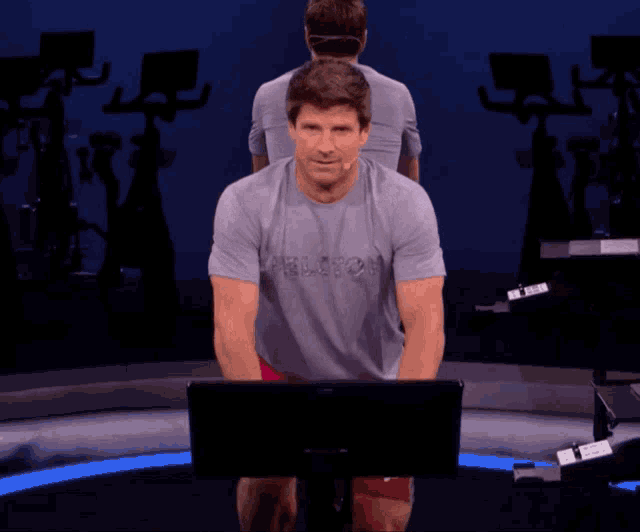 a man wearing a peloton shirt is standing in front of a computer