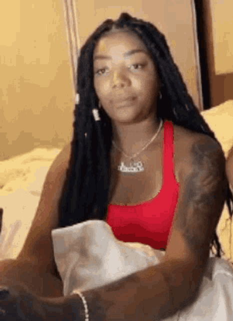 a woman with dreadlocks is sitting on a bed with a cell phone .