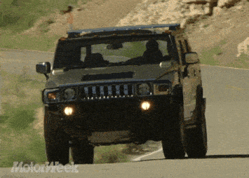 a hummer is driving down a road with a motorweek logo behind it