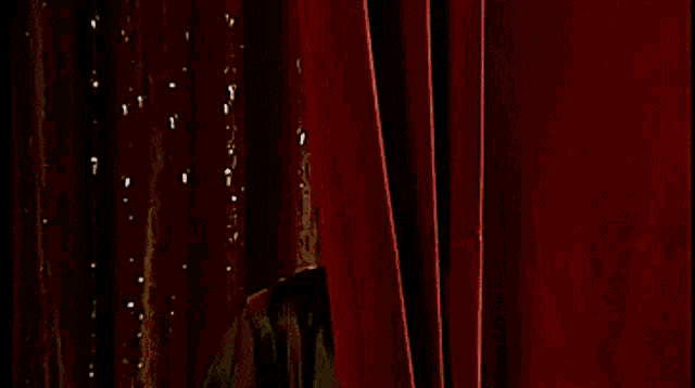 a man in a tuxedo peeking out from behind a red curtain .