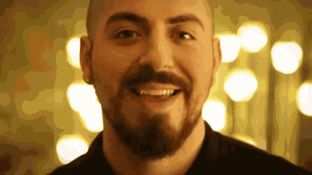 a bald man with a beard is smiling in front of a blurry background of lights