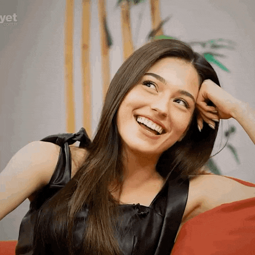 a woman is sitting on a red couch and smiling with the website yet.com.tr visible in the background