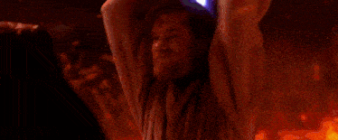 a man is holding a lightsaber in a dark room with a fire in the background .