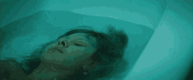 a woman laying in a bathtub with a blue light behind her
