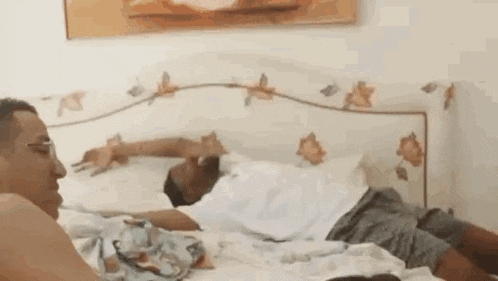 two men are laying on a bed talking to each other and one of them is smoking a cigarette .