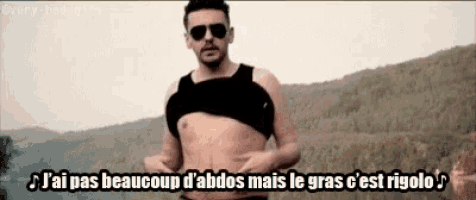 a man without a shirt is standing in front of a mountain and holding his belly .