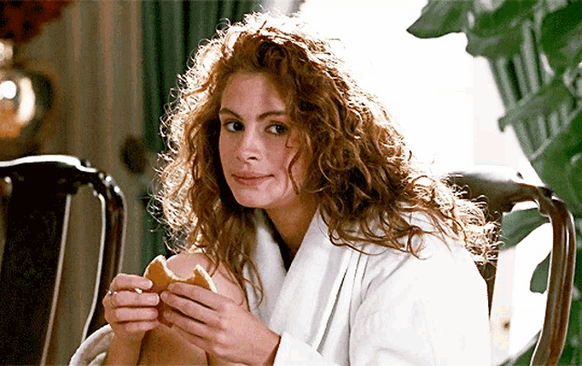 a woman with curly hair is sitting in a chair holding a sandwich