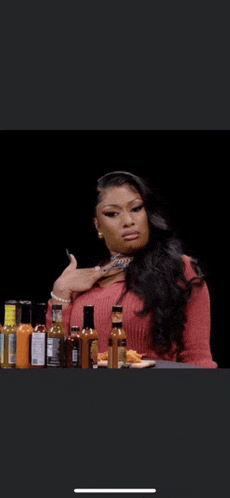 a woman is sitting at a table with bottles of hot sauce .