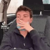 a man is sitting in a car smoking a cigarette .