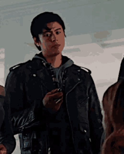 a young man in a black leather jacket is holding a cell phone