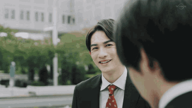 a man in a suit and tie is smiling while talking to another man in a suit