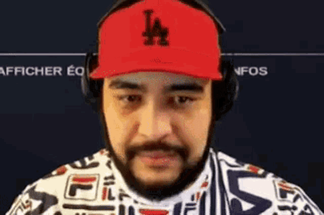 a man with a beard is wearing a red la hat and headphones .