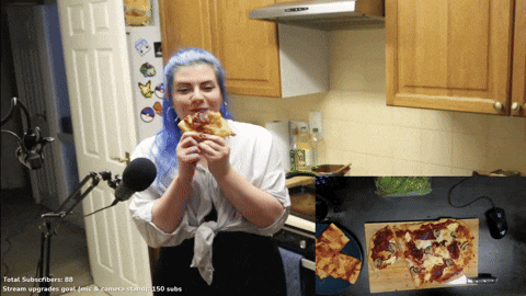 a woman with blue hair is eating a pizza in a kitchen