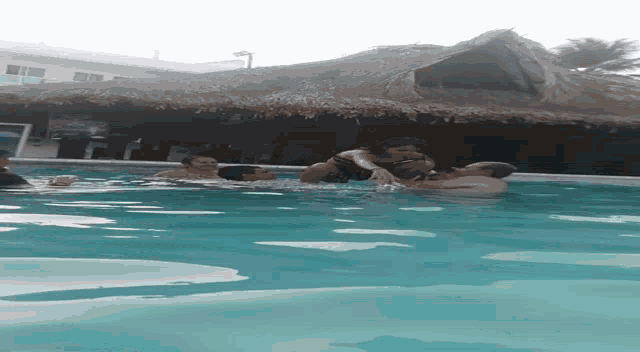 a group of people are swimming in a pool with thatched roofs
