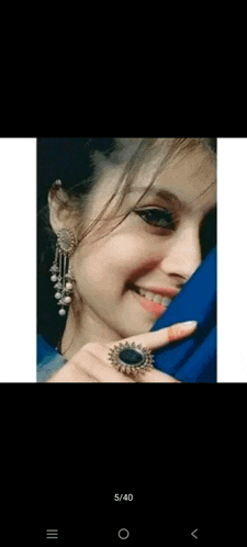 a woman wearing earrings and a ring is smiling and covering her face with her hand .