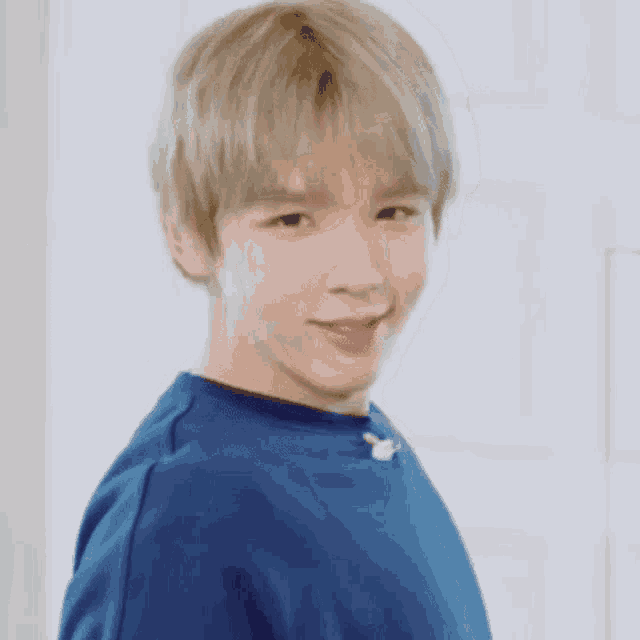 a young man with blonde hair and pink lips is wearing a blue shirt and making a funny face .