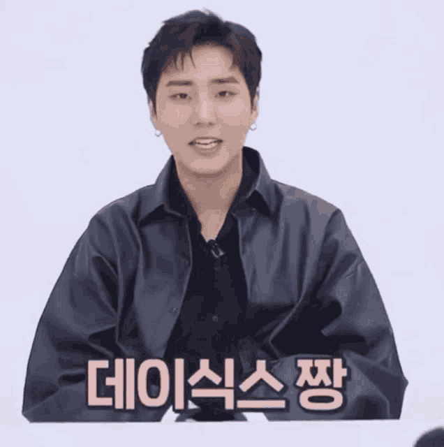 a young man wearing a black leather jacket and a black shirt is talking in a foreign language