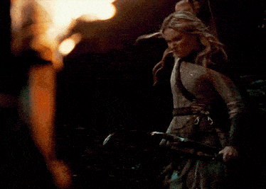 a woman is holding a bow and arrow in front of a flame