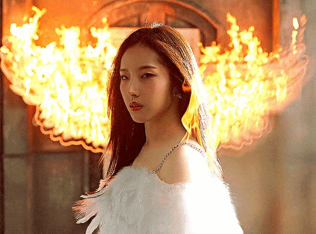 a woman in a white dress is standing in front of a wall with flames behind her