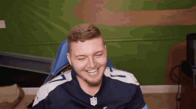 a man is sitting in a chair and smiling while wearing a blue and white nfl jersey .