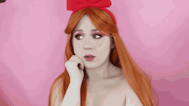 a woman with red hair and freckles is wearing a red bow on her head and making a sad face .
