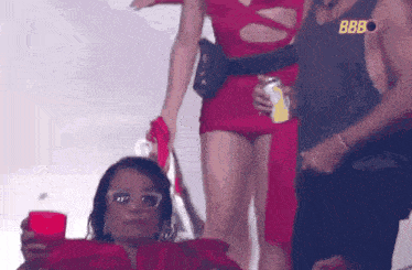 a woman in a red dress is holding a red cup while standing next to a man in a bbbo tank top .