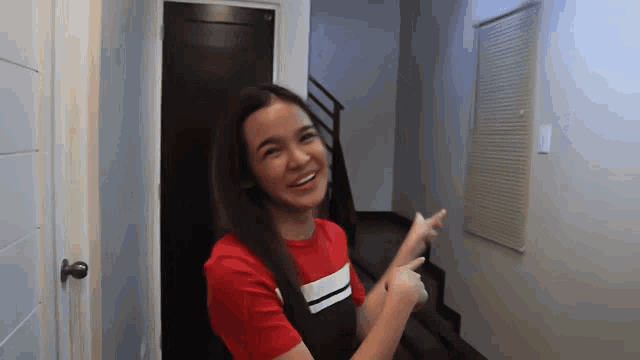 a woman in a red shirt points to a door