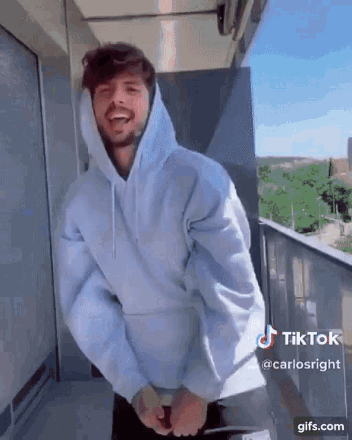 a man wearing a blue hoodie is standing on a balcony and laughing .