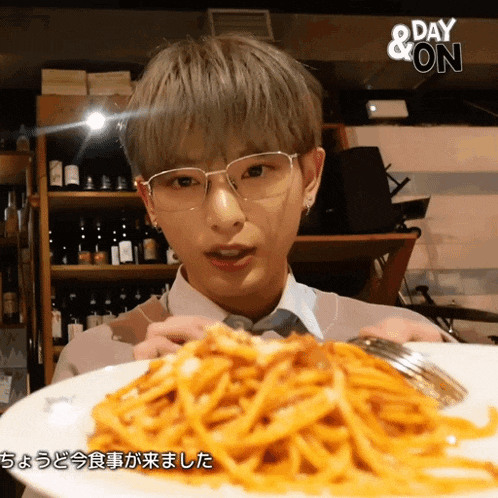 a man wearing glasses holds a plate of spaghetti in front of a sign that says " day & on "