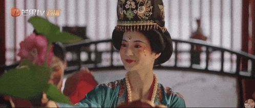 a woman in a traditional costume is holding a plant in front of a sign that says ' tv ' on it