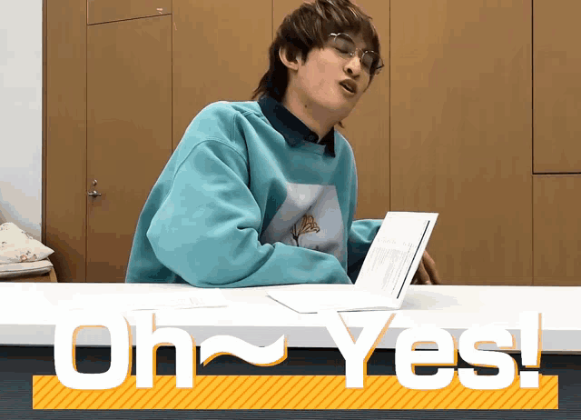 a man in a blue sweater is sitting at a table with the words oh yes