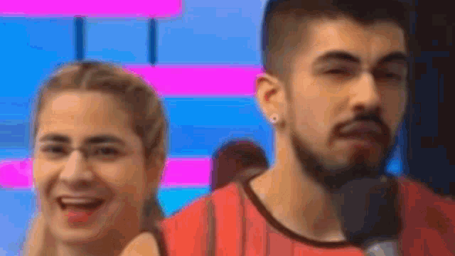 a man with a beard is talking into a microphone while a woman laughs behind him .