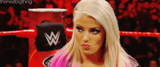 a woman with blonde hair and pink highlights is standing in a wrestling ring making a funny face .