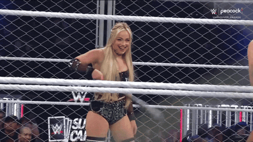 a woman in a wrestling ring behind a chain link fence that says peacock