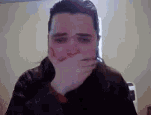 a man is covering his mouth with his hand in front of a computer screen .