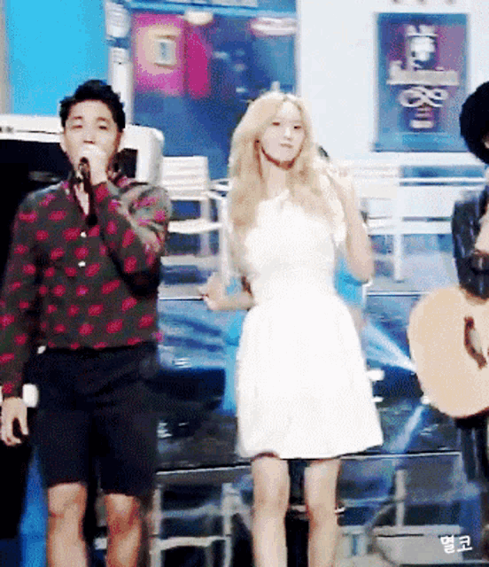 a man singing into a microphone next to a woman in a white dress holding a guitar