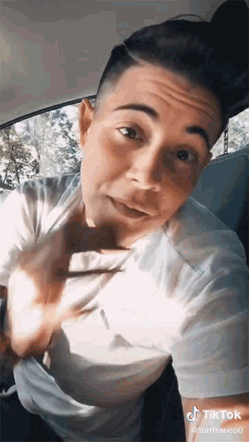 a man in a white shirt is sitting in the back seat of a car making a funny face .