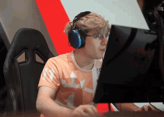 a man wearing headphones and an orange shirt with a crown on it looks at a computer screen