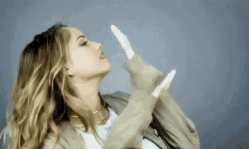 a woman is blowing a kiss with her hands in the air while wearing a jacket .